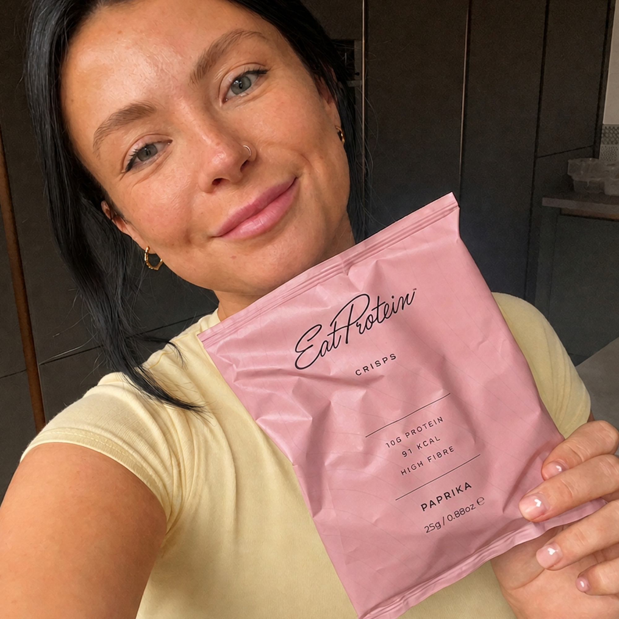 Woman holding a pack of EatProtein Paprika Protein Crisps showing 10g protein and 91 kcal