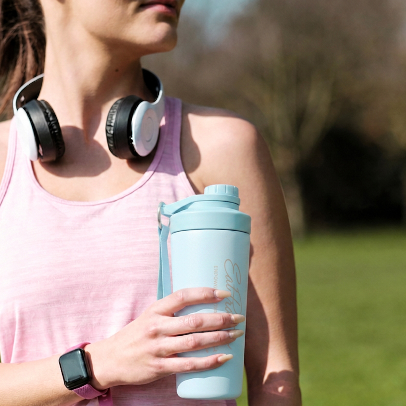 Woman with headphones round her neck, holding her EatProtein insulated bottle