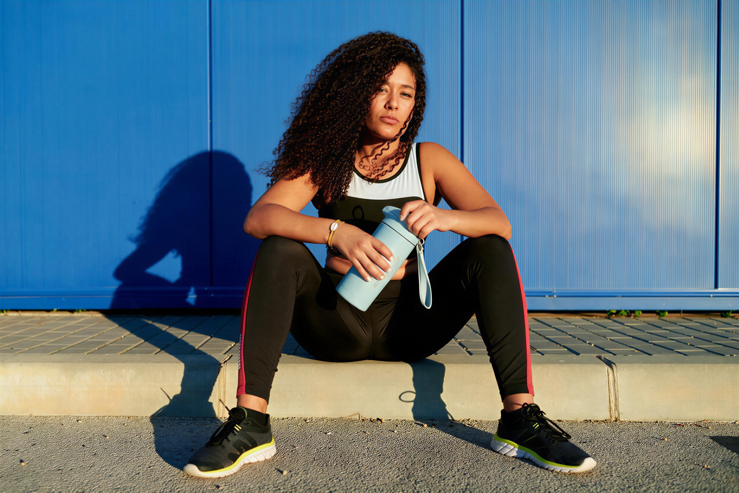Woman resting on a kerb after training, holding her EatProtein insulated bottle